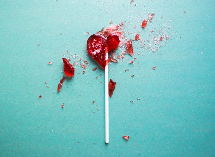 A shattered heart-shaped red lollipop against a turquoise background.