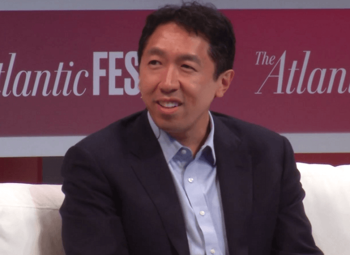 Andrew Ng in a black blazer and blue shirt sitting on stage at an event.