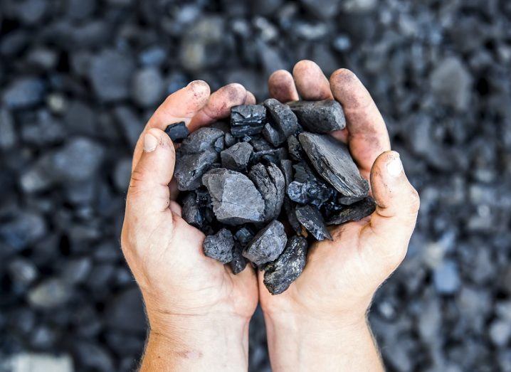 A pair of hands cupped holding coal above a coal pit.
