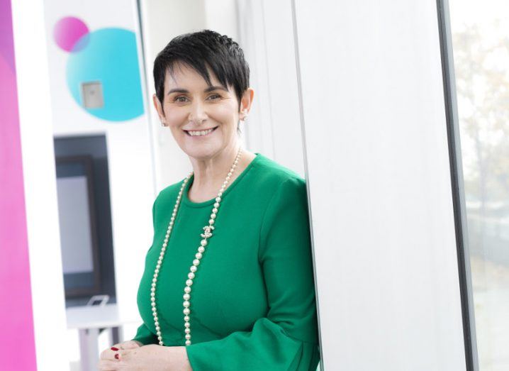 Smiling woman with short dark hair in a green dress and wearing a string of pearls.