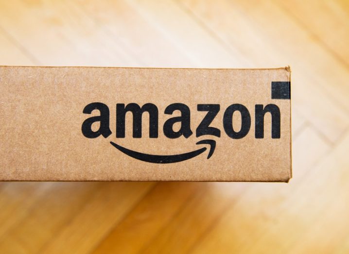 Amazon logo printed on a cardboard package, which is sitting on a parquet wood floor.