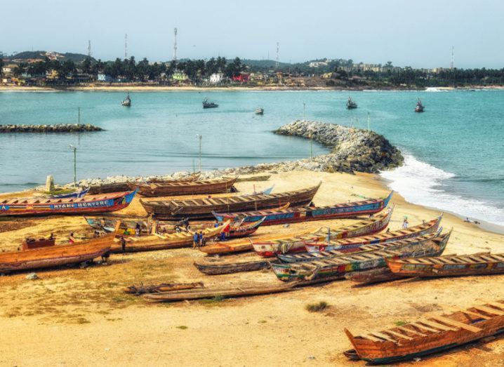 Boats on a beach at Cape Coast, Ghana, with cell towers visible in the distance.