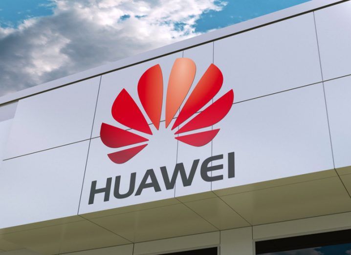 A photo of the Chinese company Huawei's logo in red on the side of a building under a blue cloudy sky.