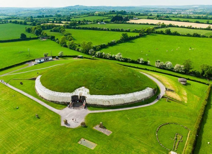 Aerial shot of the circular Newgrange site against a backdrop of green fields.