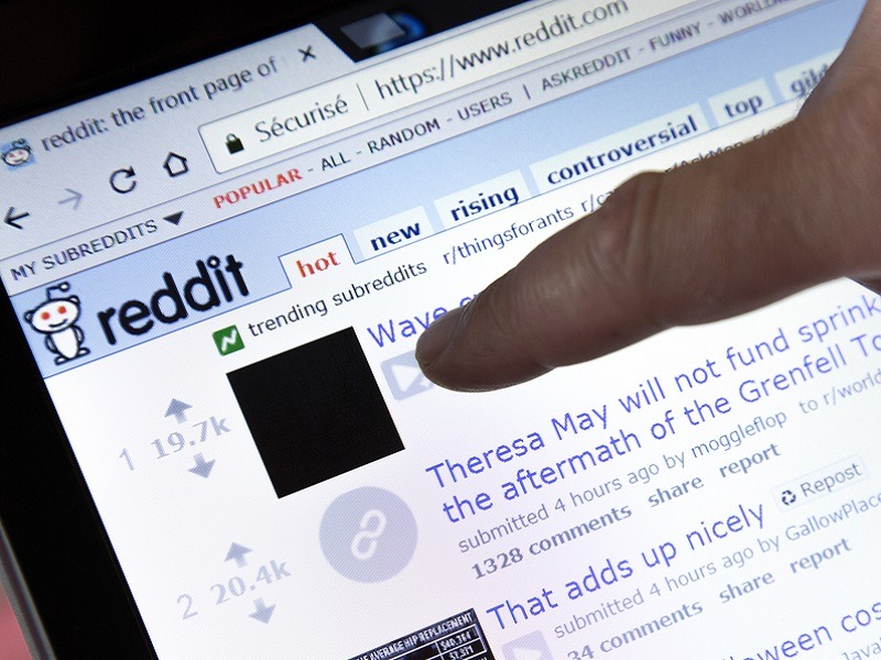Person pointing their finger at the Reddit homepage on a laptop screen.