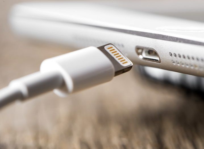 Close-up of smartphone charger cable connecting to a white smartphone on a wooden table.