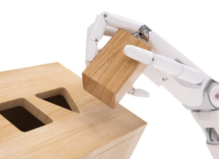 A robotic hand sorting different wooden shapes into the correct slots. Machine learning concept.