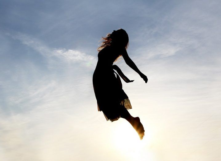 Silhouetted woman rising into the sky against a sunny background.