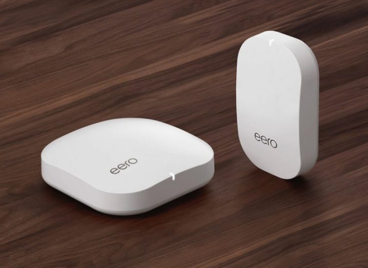 Two white Eero routers resting on dark wood surface. Devices are small and round.