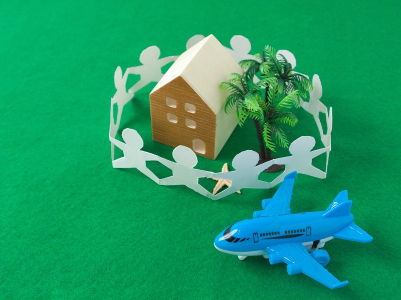Mini toy house surrounded by paper cutouts of people beside a blue toy aeroplane on a model green field.