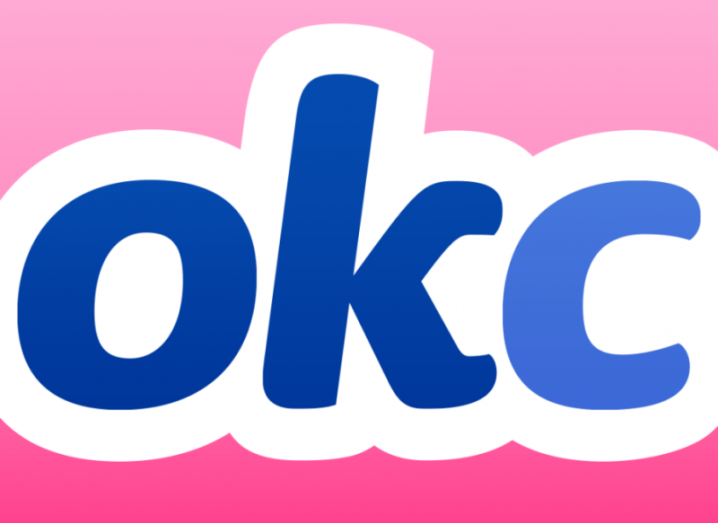 OkCupid app logo, blue writing with a white outline on a hot pink background.