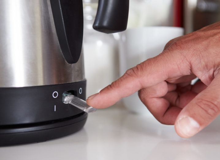 close-up of man turning on switch to boil kettle, symbolising energy usage.