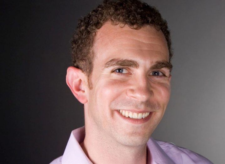 Smiling man with short curly hair in lilac shirt.