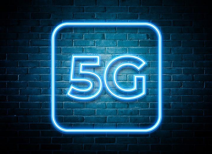 Neon blue 5G sign switched on against a brick wall.