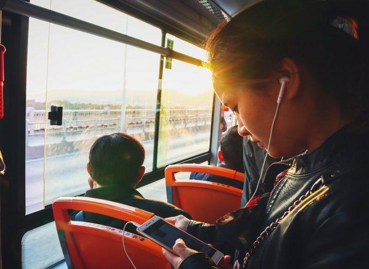 Asian woman wearing leather jacket and looking at her phone on a public bus.