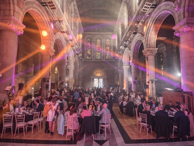 Banquet hall in Belfast with strobe lights over a room full of people sitting at tables.