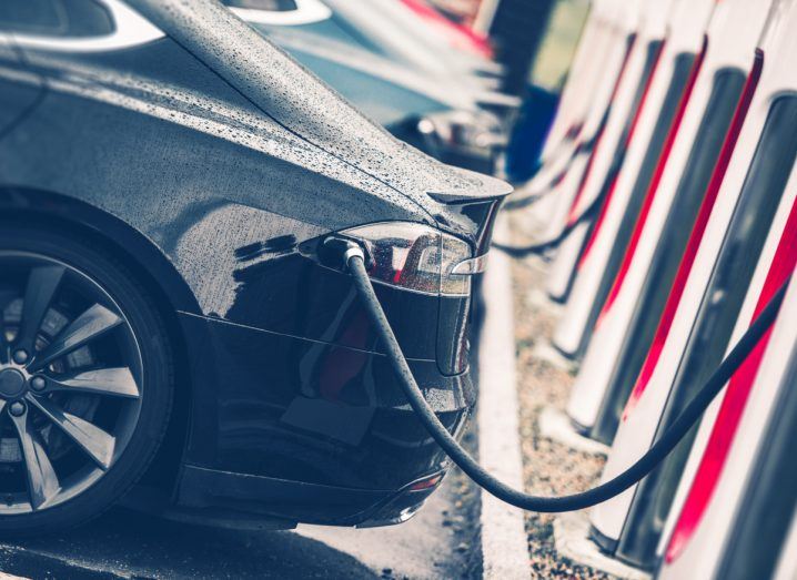 A close-up of a line of electric vehicles plugged in at a charging station.