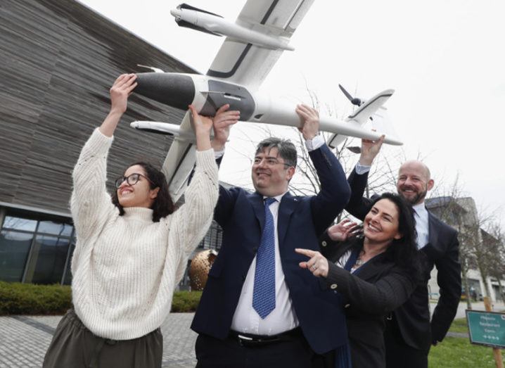 Four people hold aloft a drone outside a university.