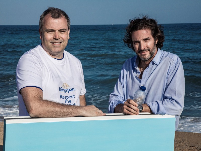 Two casually dressed men standing by the sea with one holding a plastic bottle, symbolising recycling.