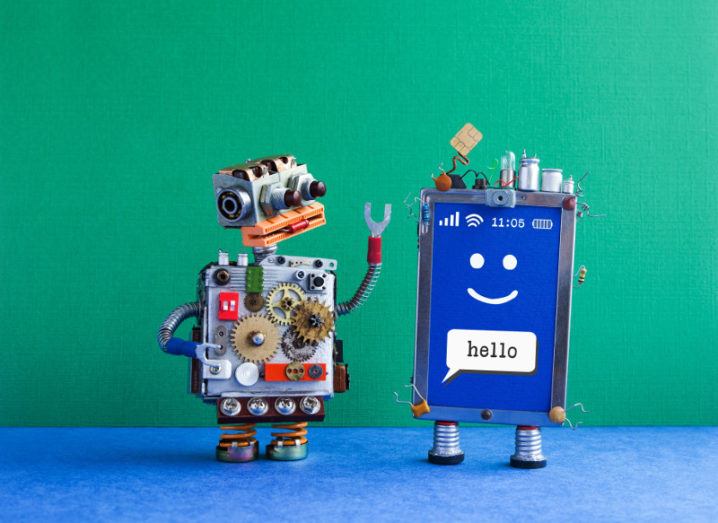 Two robots greet each other while one says hello and salutes with a SIM card for a hat against bright green background.