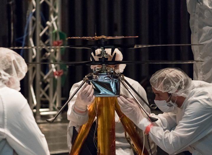 NASA researchers in white overalls tinkering with the small Mars Helicopter.