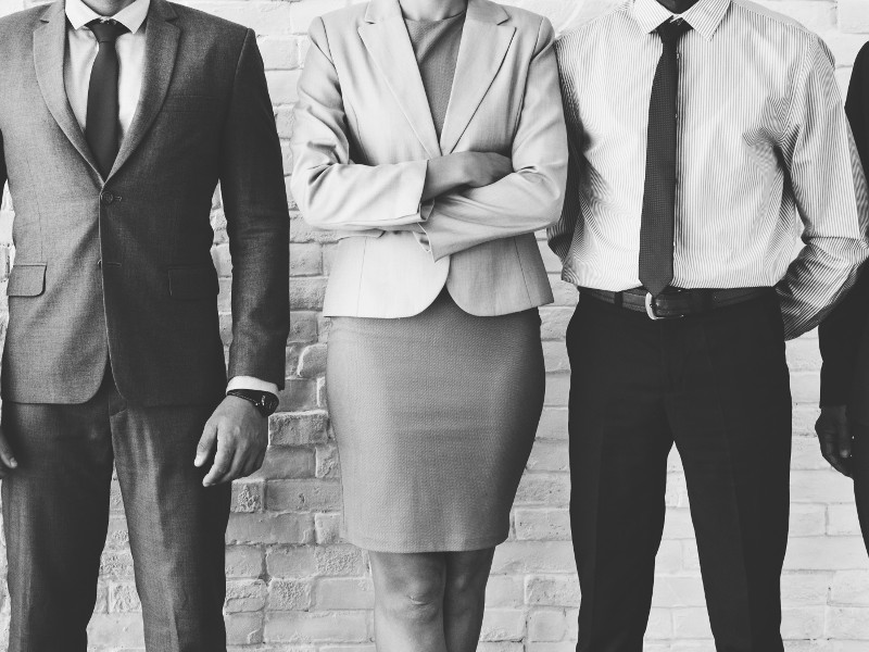 Black and white image showing a woman standing between two men, indicating the gender divide in entrepreneurship.