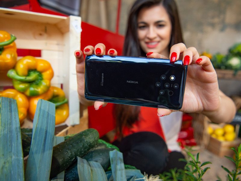 Woman in red jumper takes picture of plants using the new Nokia 9 Pureview with five cameras.