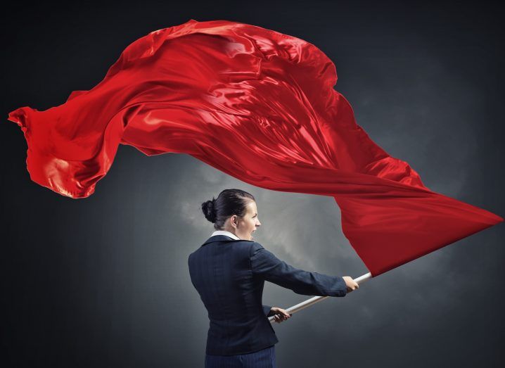 Young determined businesswoman with red flag in hands, symbolising revolution.