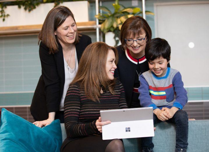Three women and a young boy sit around a computer smiling.
