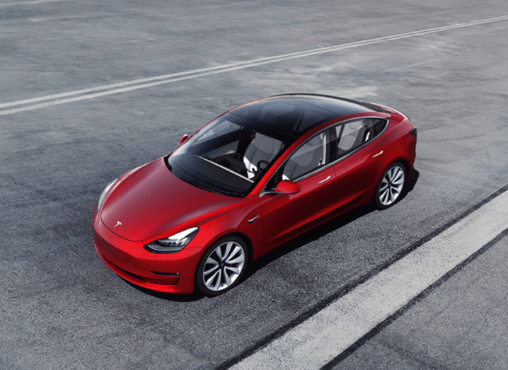 Picture of a red Tesla Model 3 on a grey asphalt surface.
