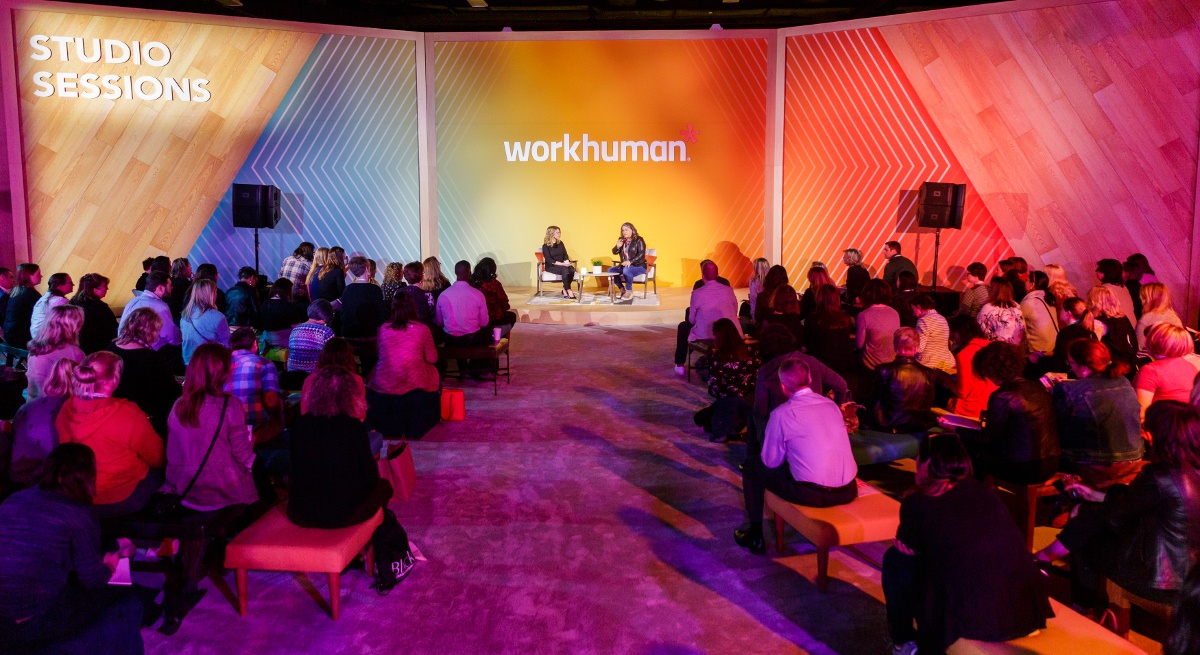 A shot of a small stage with the two women sitting in front of an audience. The Workhuman logo is behind them.