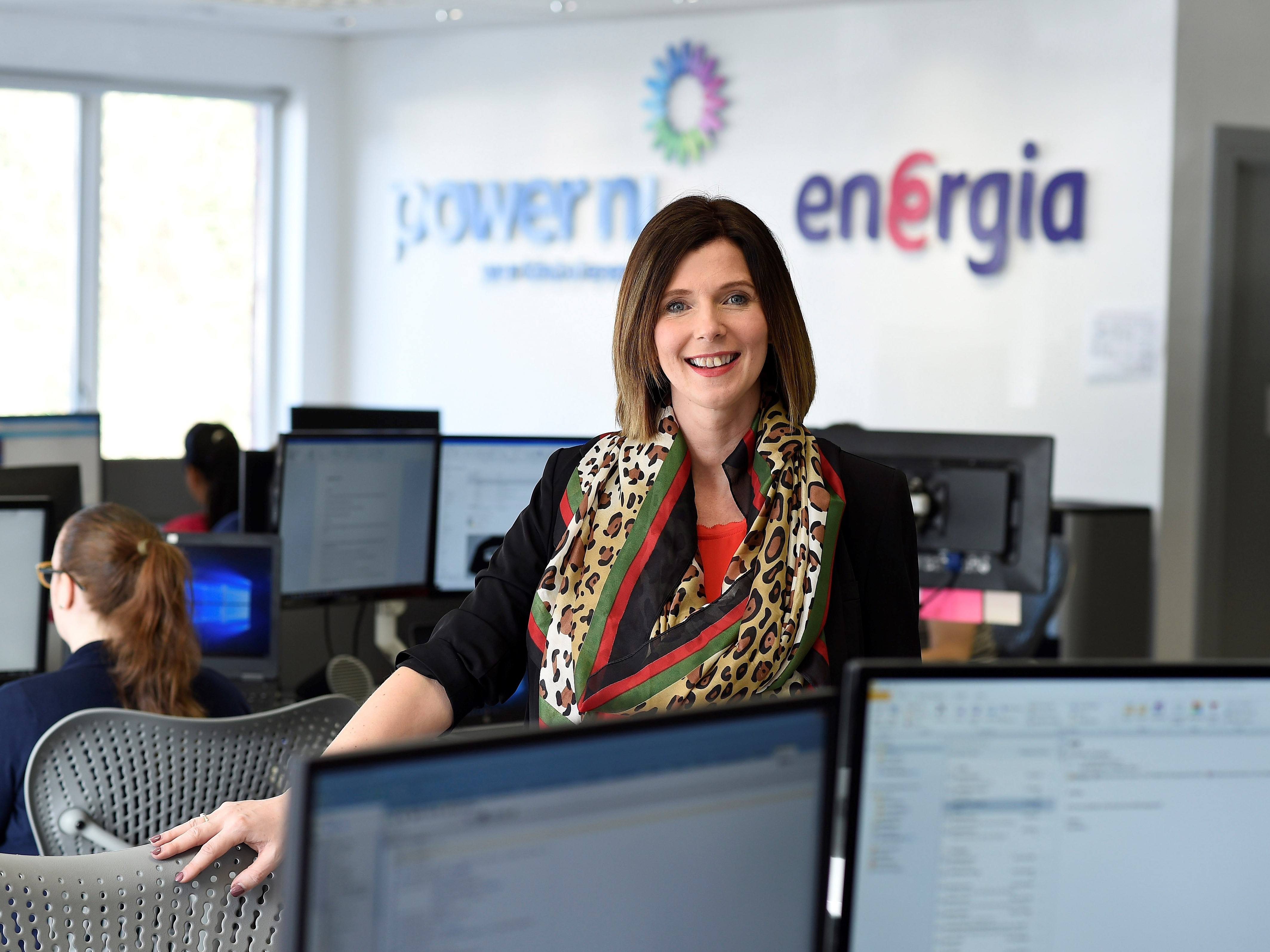 Woman with black hair and leopard print scarf standing in a busy office.