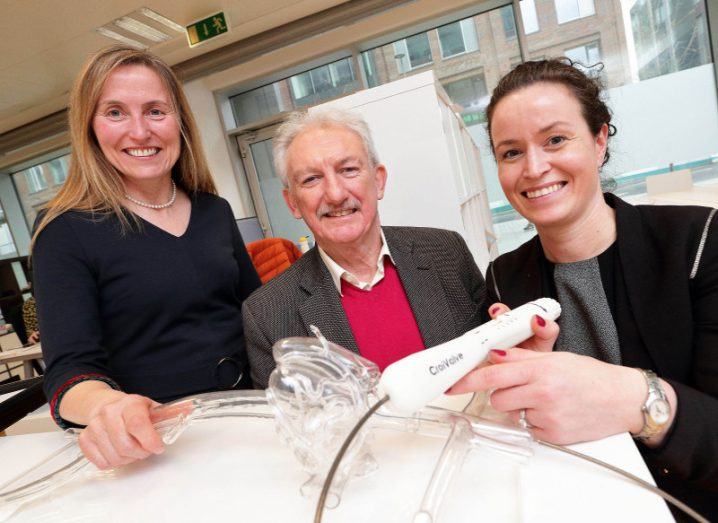 Two women and a man hold a medical device.