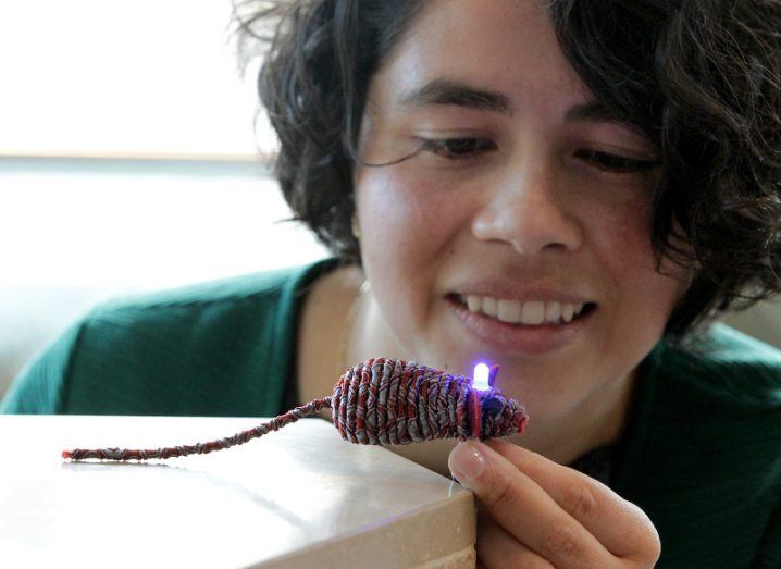Andrea Pacheco holds and peers at a small woven mouse with a lit-up LED on its head.