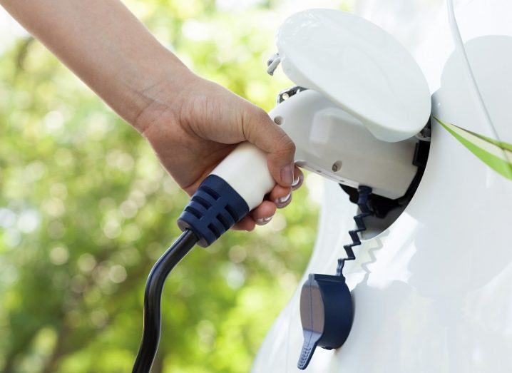 Arm connecting an EV charger cable to a car against a forest background.