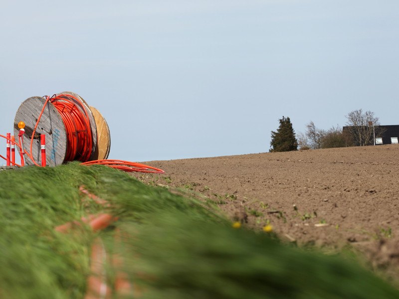 A roll of bright orange fibre cable on top of a hill going towards a rural home.
