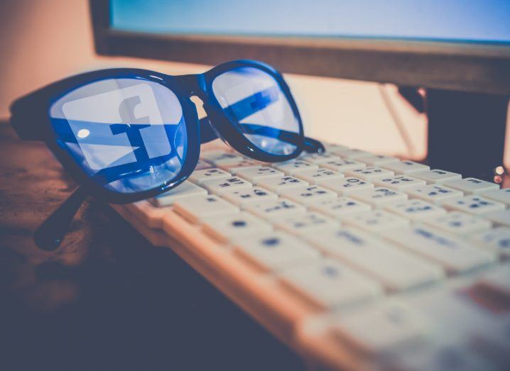 Facebook logo reflection on a pair of glasses resting on a computer keyboard.
