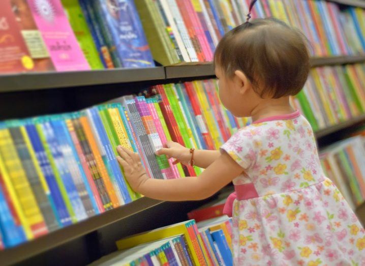 Young child looking at a multicoloured collection of children's books on a shelf.