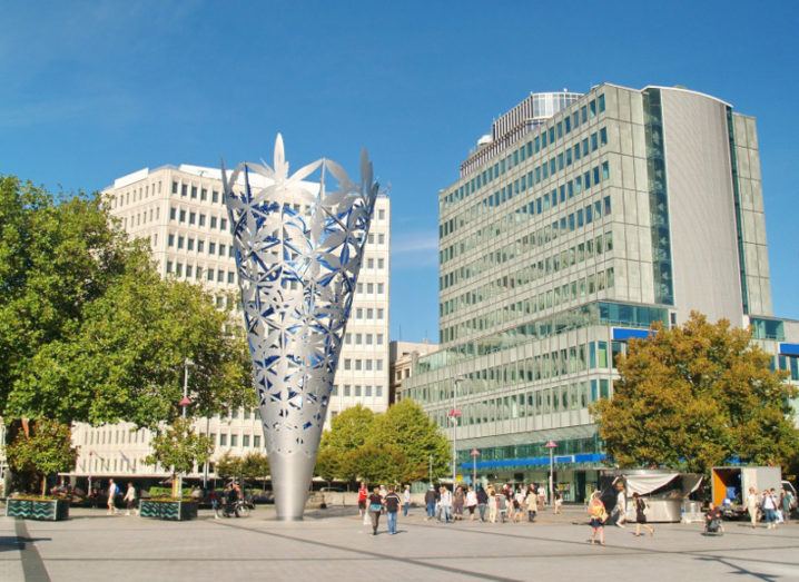 A picture of a monument in a square in Christchurch, New Zealand, under a blue sky surrounded by modern buildings.
