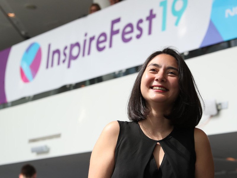 Young dark haired woman standing in front of an Inspirefest 19 sign.