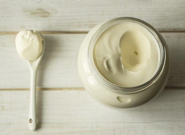 Mayonnaise in a glass jar with a spoon on white wooden boards.