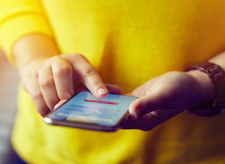 Close-up of the hands of a person in a bright yellow jumper paying for something using her mobile phone.