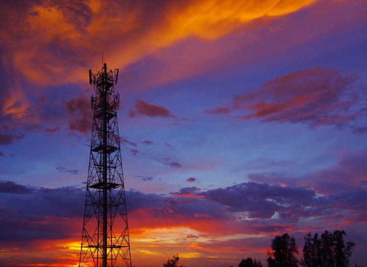 View of a cell tower telecoms infrastructure against a purple, orange and periwinkle sunset.