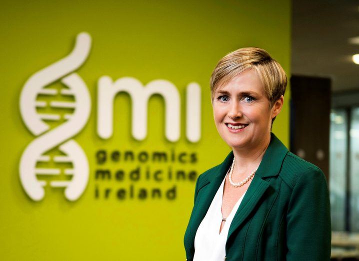 Woman with blonde short hair wearing a green suit and white blouse in front of lime green wall with GMI logo in white.