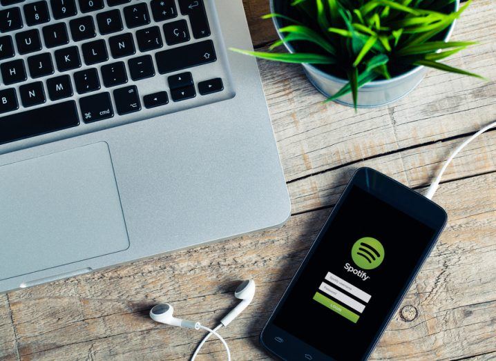 An Apple computer on a desk beside a mobile phone that is running Spotify.