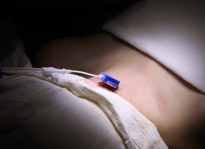 Close-up of a small blue sensor on a patient lit up by a light surrounded by darkness.