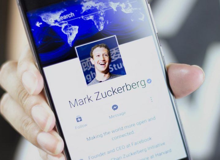 Person holding a phone screen showing the Facebook profile of Mark Zuckerberg.