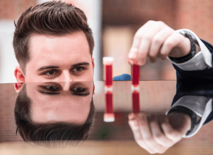 Student Entrepreneur of the Year Christopher McBrearty places blood test vials on a tabletop that reflects his face.