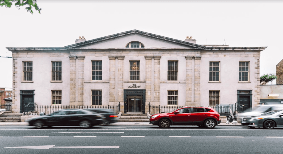 A grey building is facing the camera on the side of a street in the city centre