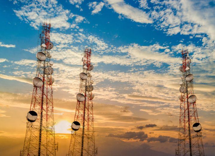 View of telecommunications towers in red standing high against sunrise and cloud-streaked sky.